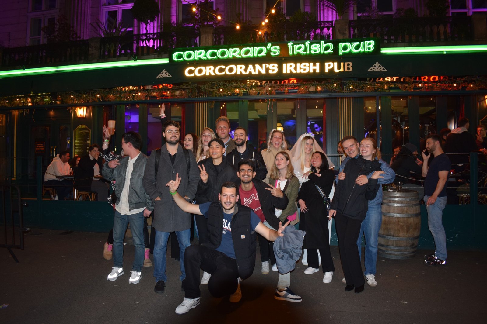 Eine lächelnde Pub-Crawl-Gruppe posiert nachts vor einem Pub in Paris